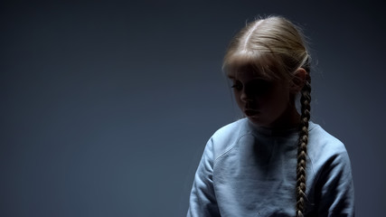 Depressed kid standing alone in darkness, bullying and violence victim concept