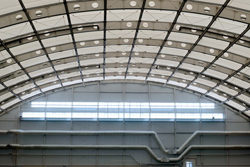 Semicircular roof inside a large room. Technical or sports facility. Hangar or gym. Pipes and communications. Transparent ceiling.