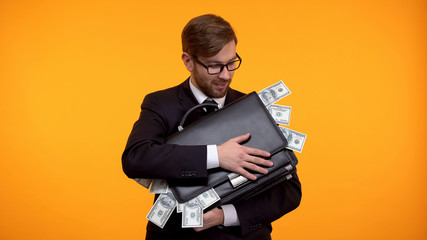 Businessman holding briefcase full of money, isolated on yellow background - obrazy, fototapety, plakaty