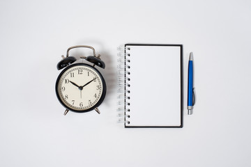  Retro alarm clock next to a pen and notebook on a white background. Studying at school and university. Good morning. Deadline. Business