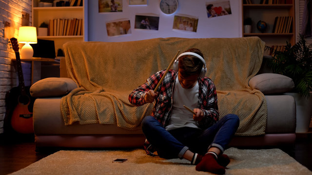 Boy in headset listening to music in his room and imaging that playing drums