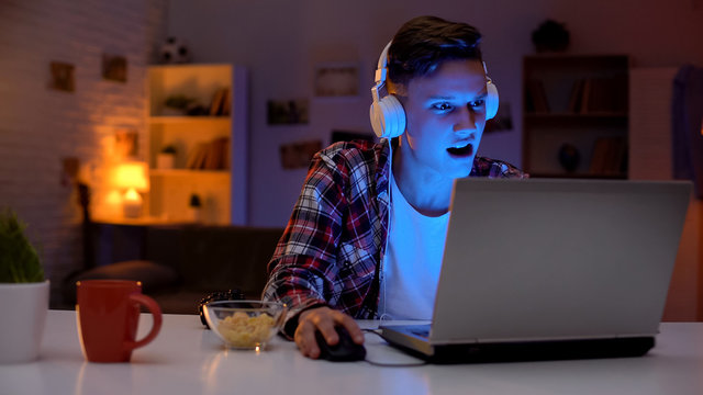 Overemotional Teen Playing Computer Game On Laptop And Eating Snacks, Addiction