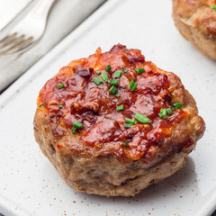 Low carb paleo meat cups, stuffed with champignons, bacon and cheese, garnished with green onion, on  white plate, square format, closeup
