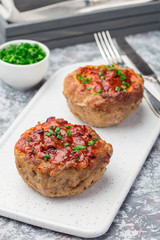 Low carb paleo meat cups, stuffed with champignons, bacon and cheese, garnished with green onion, on white plate, vertical