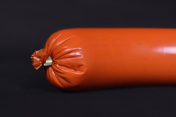 End of orange sausage in synthetic casing on black background