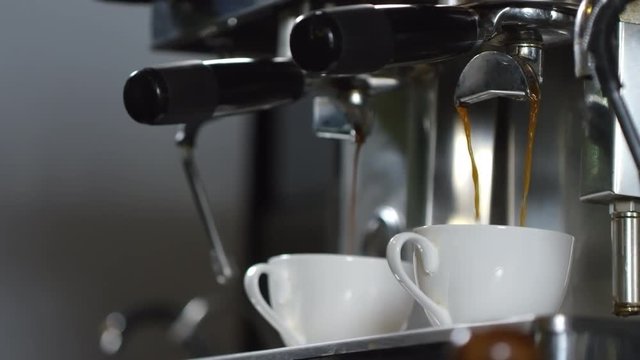 Close-up shot of single and double shots of espresso being poured into white cups at the same time on professional coffee machine, with its blurred metal surface in background