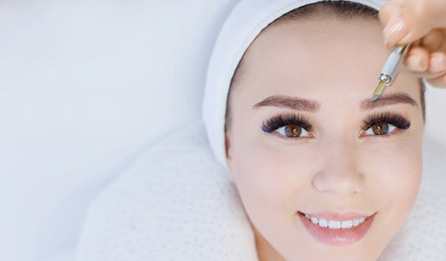 Beautiful young girl with long eyelashes tweezing her eyebrows in a beauty salon. Woman doing eyebrow permanent makeup correction . Microblading brow.