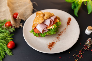 Breakfast croissant sandwich with ham and cheese. Top view. black background with vegetables. Slow-mo.