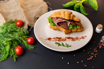 Breakfast croissant sandwich with bacon and tomatoes. Top view. black background with vegetables. Slow-mo