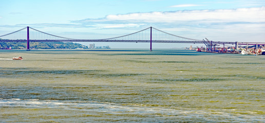 Fototapeta na wymiar 25 de Abril suspension bridge across the River Tagus in Lisbon, Portugal, with the Monument of the Discoveries in the background