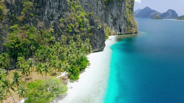 Aerial drone view of pristine tropical white sand beach surrounded by karst rocky cliffs and turquoise sea on Pinagbuyutan Island. El Nido, Palawan, Philippines. Breathtaking landscape