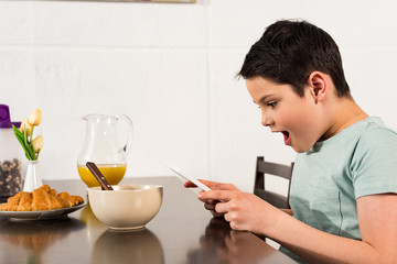 shocked boy using digital tablet during breakfast in kitchen