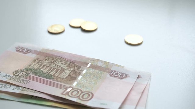 To count money. Money falls on a white table. People hand quickly throws russian rubles banknotes nominals 200 and 100 and coins nominal 10 on a white background