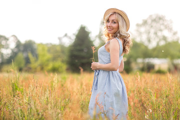 Fototapeta na wymiar Rural, rural life. Walking through the meadow blonde young woman in a hat. Summertime.