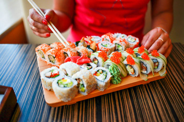 girl with well-groomed hands holds chopsticks for sushi. Girl eats a large set of sushi.