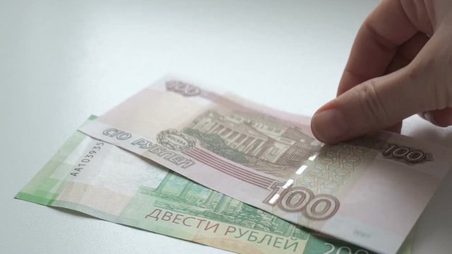 To count money. Hands recount banknotes on a white table. People hand lays out russian rubles banknotes nominals 200 and 100 on a white background
