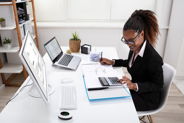 Smiling Businesswoman Calculating Invoice On Computer