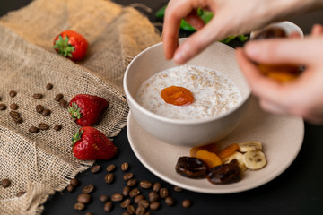Tasty breakfast. Top view of a bowl of muesli with oats, nuts and dried fruit on black table. Slow-mo.