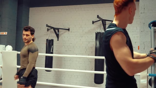 Two young professional fighters are warming before training making leg swings on ringside in fight club. Athletes and sport concept.