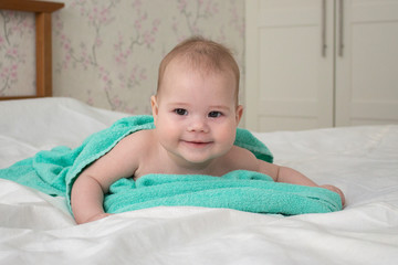 Laughing baby kid lies wrapped in a towel after bathing. joyful positive girl boy naughty look. Baby portrait soft focus