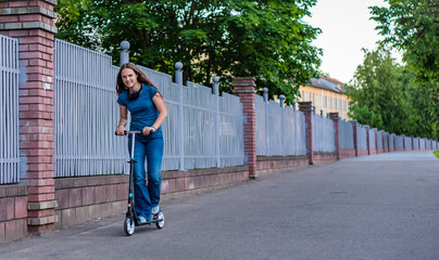 Outdoor portrait of young teenager brunette girl with long hair driving scooter on city street