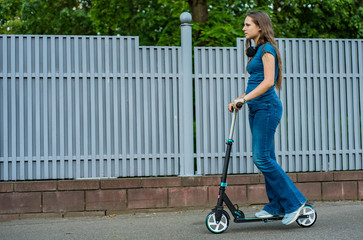 Outdoor portrait of young teenager brunette girl with long hair driving scooter on city street