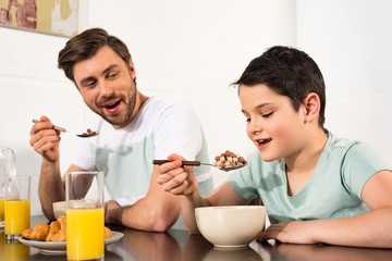 smiling father and son eating breakfast cereal in kitchen