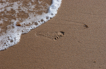 Footprint on a wet, sandy beach. Water is washing upp, about to erase the print.