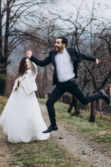 A stylish and charismatic groom jumps up holding his attractive smiling bride. Cool couple of newlyweds photographed in a jump, emotional dynamic photo of brides