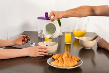 cropped view of dad pouring milk in bowl during breakfast with son
