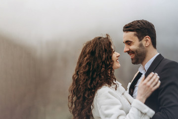 Happy smiling couple of husband and wife. The bride and groom standing next to each other during a photo shoot on a walk in misty weather in the mountains