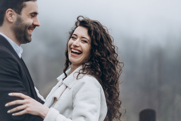 Happy smiling couple of husband and wife. The bride and groom standing next to each other during a photo shoot on a walk in misty weather in the mountains