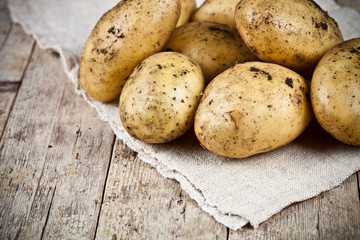 Fresh organic dirty potatoes heap closeup on linen tablecloth on rustic wooden background.