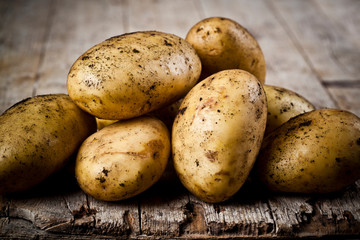 Newly harvested dirty potatoes heap on rustic wooden background.