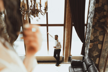 A man stands by the window with a glass of alcohol, and on whom is the future bride from the second floor of the house watching