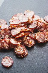 Thinly sliced sausage slices on a black stone board. 