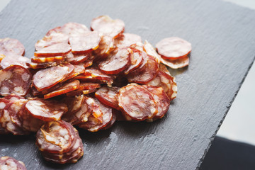 Thinly sliced sausage slices on a black stone board. 