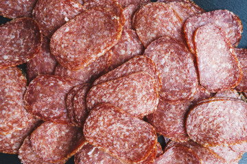 Thinly sliced sausage slices on a black stone board. 