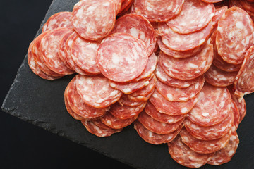 Thinly sliced sausage slices on a black stone board. 