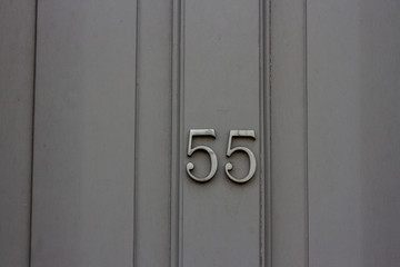 House number 55 with the fifty-five on a gray door in silver metal numbers