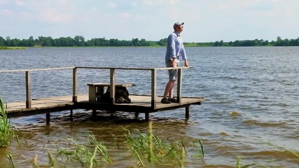 man stands on a pier at the lake in windy weather