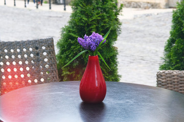 Vase with purple flowers is on the table in summer cafe on the street. Design of restaurant.