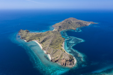 Fototapeta na wymiar Seen from a bird's eye view, an idyllic island is surrounded by a healthy coral reef in Komodo National Park, Indonesia. This tropical area is known for its marine biodiversity as well as its dragons.