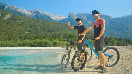 Young guys on ebikes stand by the river and look at the beautiful landscape.