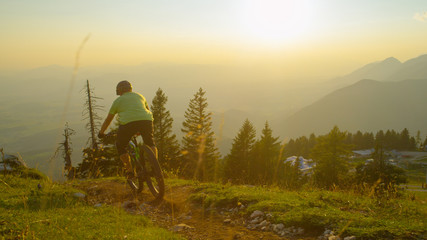 LENS FLARE: Unrecognizable man rides his mountain bike downhill at sunset.