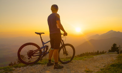 Naklejka na ściany i meble COPY SPACE: Unrecognizable man watches the sunrise before a mountain bike ride.