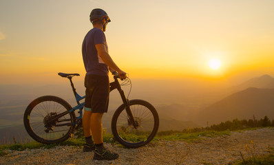 SUN FLARE Man stands next to his mountain bike while observing the sunlit nature