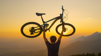 Fototapeta na wymiar CLOSE UP: Unrecognizable man lifts his bicycle in the air at golden sunset.