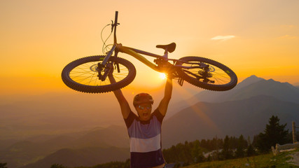 LENS FLARE Morning sun rays shine on the excited man lifting his bike above head