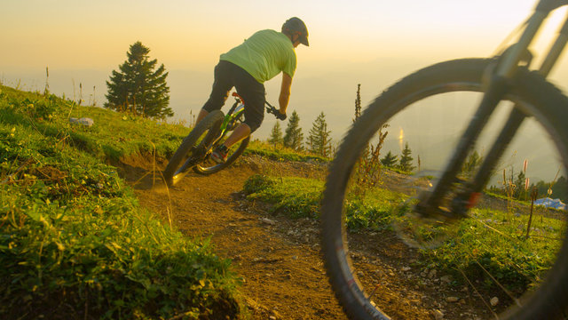 CLOSE UP: Golden sunbeams shine on mountain bikers riding down dirt trail.